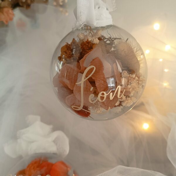 Boule de Noël en verre personnalisée avec prénom, remplie de fleurs séchées naturelles et décorée sur le dessus, idéale pour embellir le sapin et apporter une touche festive et élégante. Décoration de sapin de Noël originale, boule personnalisée en verre avec prénom gravé, contenant des fleurs séchées colorées, parfaite pour une ambiance chaleureuse et authentique. Boule de Noël artisanale en verre, personnalisable avec prénom, garnie de fleurs séchées à l’intérieur, un ornement raffiné pour sapin de Noël et décoration festive de fin d’année. Boue de noël pour mon 1er noël, joyeux noël , belles fêtes de fin d'année, cadeau à personnaliser, idée cadeau fait main à personnaliser avec prénom ou meesage. Ornement de Noël en verre transparent, boule personnalisée avec prénom et fleurs séchées, une décoration unique et naturelle pour sapin de Noël traditionnel ou moderne. Merry Christmas