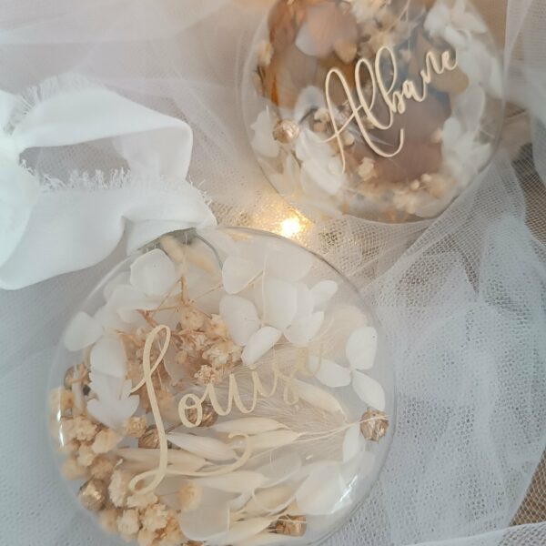 Boule de Noël en verre personnalisée avec prénom, remplie de fleurs séchées naturelles et décorée sur le dessus, idéale pour embellir le sapin et apporter une touche festive et élégante. Décoration de sapin de Noël originale, boule personnalisée en verre avec prénom gravé, contenant des fleurs séchées colorées, parfaite pour une ambiance chaleureuse et authentique. Boule de Noël artisanale en verre, personnalisable avec prénom, garnie de fleurs séchées à l’intérieur, un ornement raffiné pour sapin de Noël et décoration festive de fin d’année. Boue de noël pour mon 1er noël, joyeux noël , belles fêtes de fin d'année, cadeau à personnaliser, idée cadeau fait main à personnaliser avec prénom ou meesage. Ornement de Noël en verre transparent, boule personnalisée avec prénom et fleurs séchées, une décoration unique et naturelle pour sapin de Noël traditionnel ou moderne. Merry Christmas