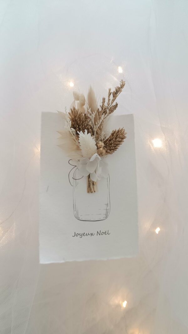 Carte de vœux artisanale “Merveilleuse Année” présentée dans une mise en scène poétique. Sur un fond doux et lumineux, la carte blanche est décorée d’un petit bouquet de fleurs séchées naturelles — pampas, blé, gypsophile et feuillages dorés — fixées au-dessus d’une illustration d’arrosoir avec un cœur. Elle repose sur une rondelle de bois entourée de plumes de pampa et de guirlandes lumineuses, créant une ambiance chaleureuse et naturelle. Carte de remerciement pour cette nouvelle année - carte à offrir personnalisé pour noël et bonne année -