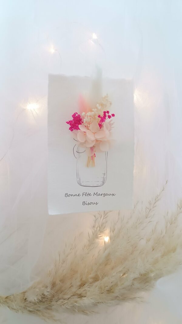 Carte de vœux artisanale “Merveilleuse Année” présentée dans une mise en scène poétique. Sur un fond doux et lumineux, la carte blanche est décorée d’un petit bouquet de fleurs séchées naturelles — pampas, blé, gypsophile et feuillages dorés — fixées au-dessus d’une illustration d’arrosoir avec un cœur. Elle repose sur une rondelle de bois entourée de plumes de pampa et de guirlandes lumineuses, créant une ambiance chaleureuse et naturelle. Carte de remerciement pour cette nouvelle année - carte à offrir personnalisé pour noël et bonne année -