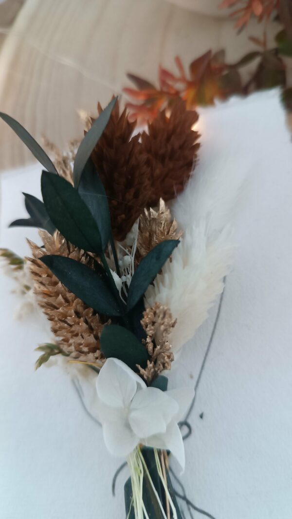 Carte de vœux artisanale “Merveilleuse Année” présentée dans une mise en scène poétique. Sur un fond doux et lumineux, la carte blanche est décorée d’un petit bouquet de fleurs séchées naturelles — pampas, blé, gypsophile et feuillages dorés — fixées au-dessus d’une illustration d’arrosoir avec un cœur. Elle repose sur une rondelle de bois entourée de plumes de pampa et de guirlandes lumineuses, créant une ambiance chaleureuse et naturelle. Carte de remerciement pour cette nouvelle année - carte à offrir personnalisé pour noël et bonne année -
